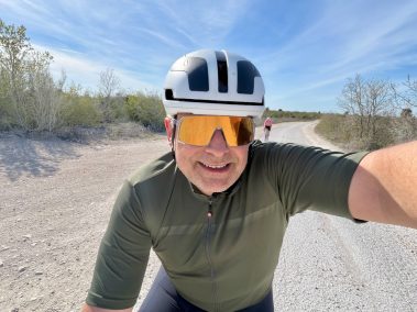 Rennradfahrer in oliv-grünem Trikot mit weißem Helm und orangefarbener Sonnenbrille macht Selfie mit der Insta360 Go Ultra