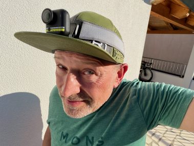 Mann mit grüner Kappe und türkisem T-Shirt macht ein Selfie mit der Insta360 Go Ultra am Bruststrapez im Freien