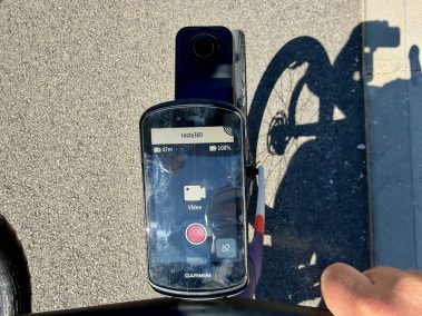 Fahrradlenker mit GPS-Computer und Insta360 Go Ultra Kamera nebeneinander montiert, Straße im Hintergrund