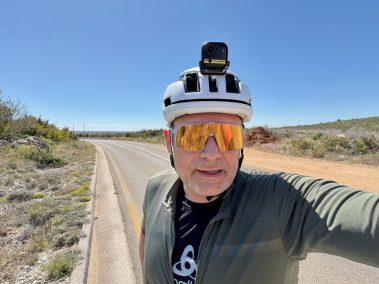Rennradfahrer-Selfie mit orangefarbenen Sonnengläsern und weißem Helm auf offener Straße, aufgenommen mit der Insta360 Go Ultra