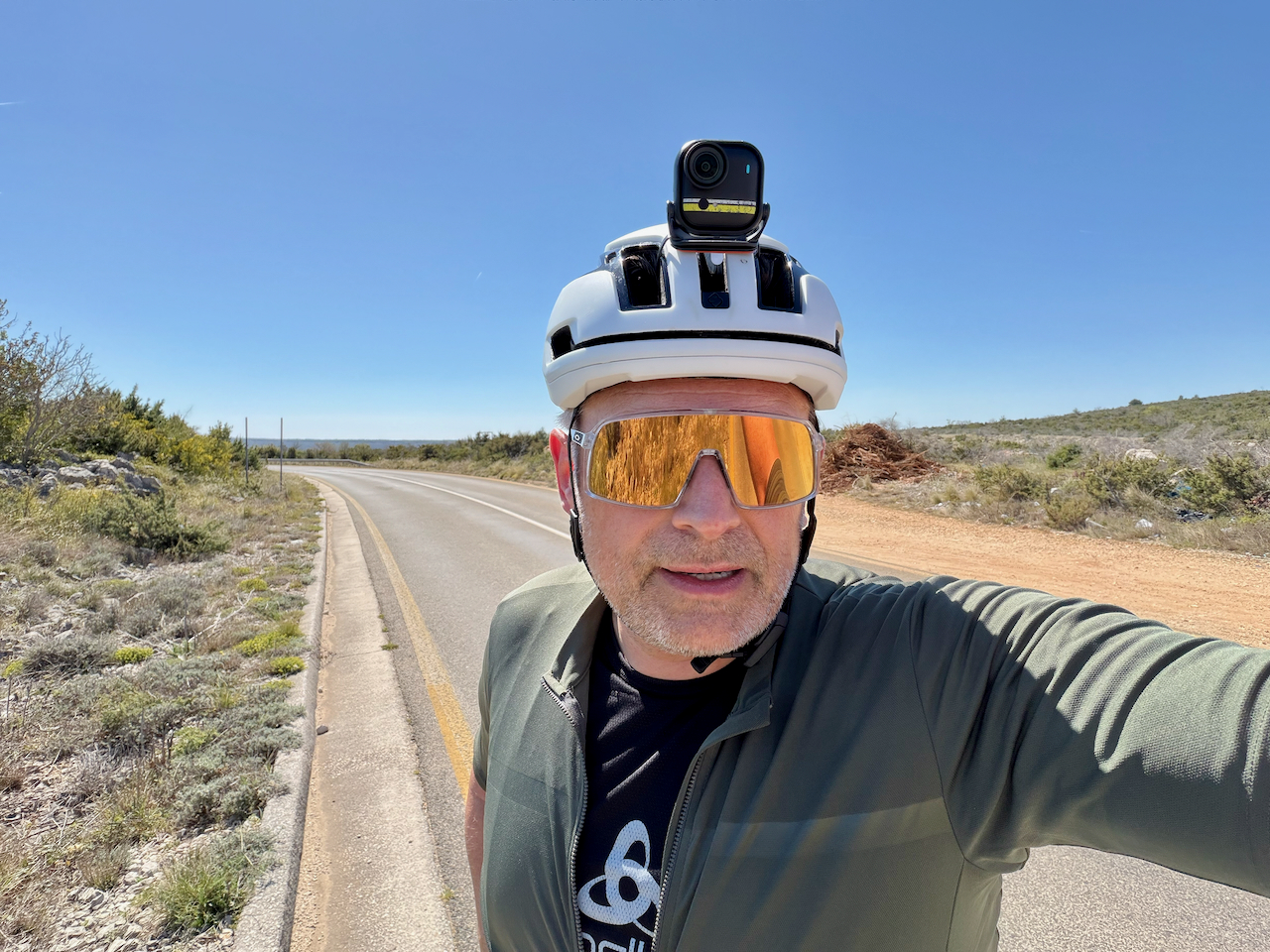 Selfie auf der Rennradtour – Insta360 Go Ultra KI-Kamera in Aktion Rennradfahrer-Selfie mit orangefarbenen Sonnengläsern und weißem Helm auf offener Straße, aufgenommen mit der Insta360 Go Ultra