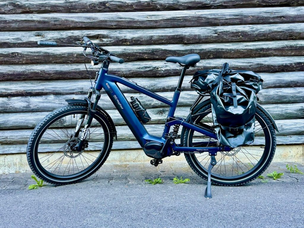 MapFour Roam blau mit Seitentasche vor rustikaler Holzwand – Touring Setup