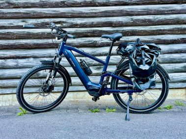 MapFour Roam blau mit Seitentasche vor rustikaler Holzwand – Touring Setup