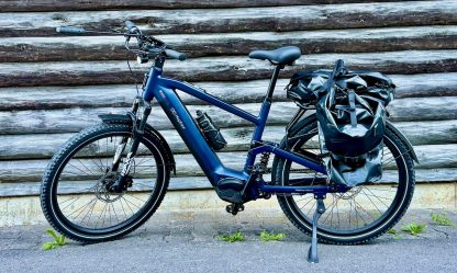 MapFour Roam blau mit Seitentasche vor rustikaler Holzwand – Touring Setup