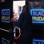Kunden drängen zur Black-Friday-Aktion in ein Geschäft mit Neonschild